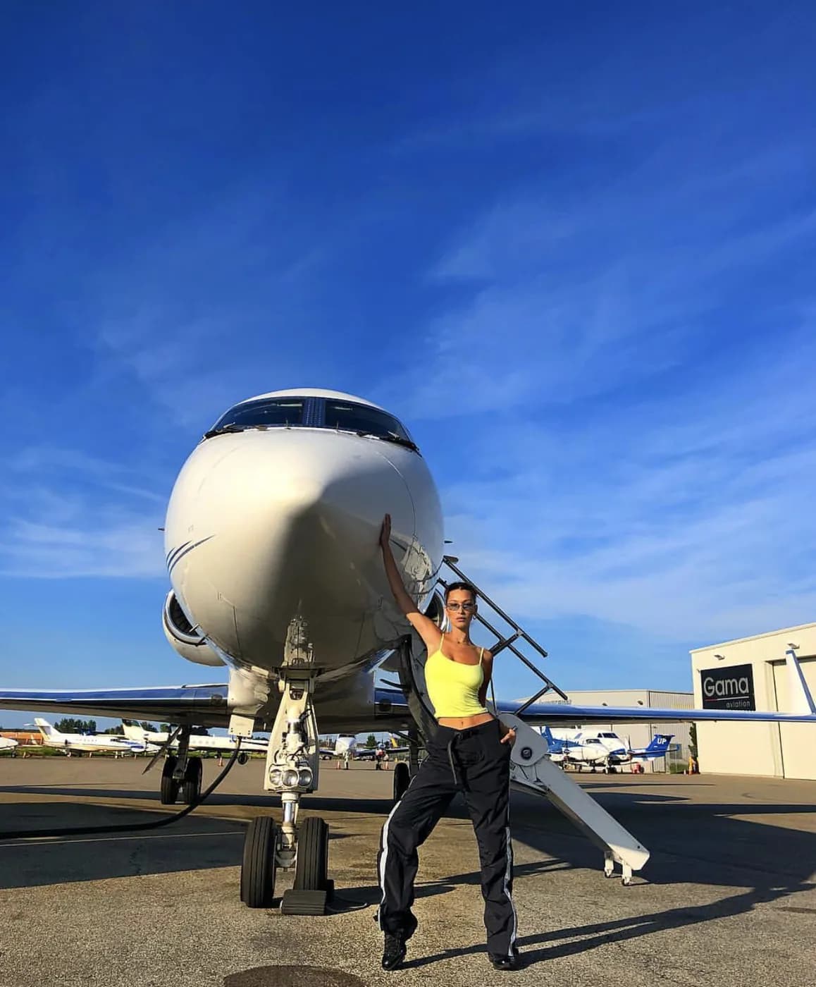 Bella Hadid at the nose of a private jet under open sky, brand photography for PRVT
