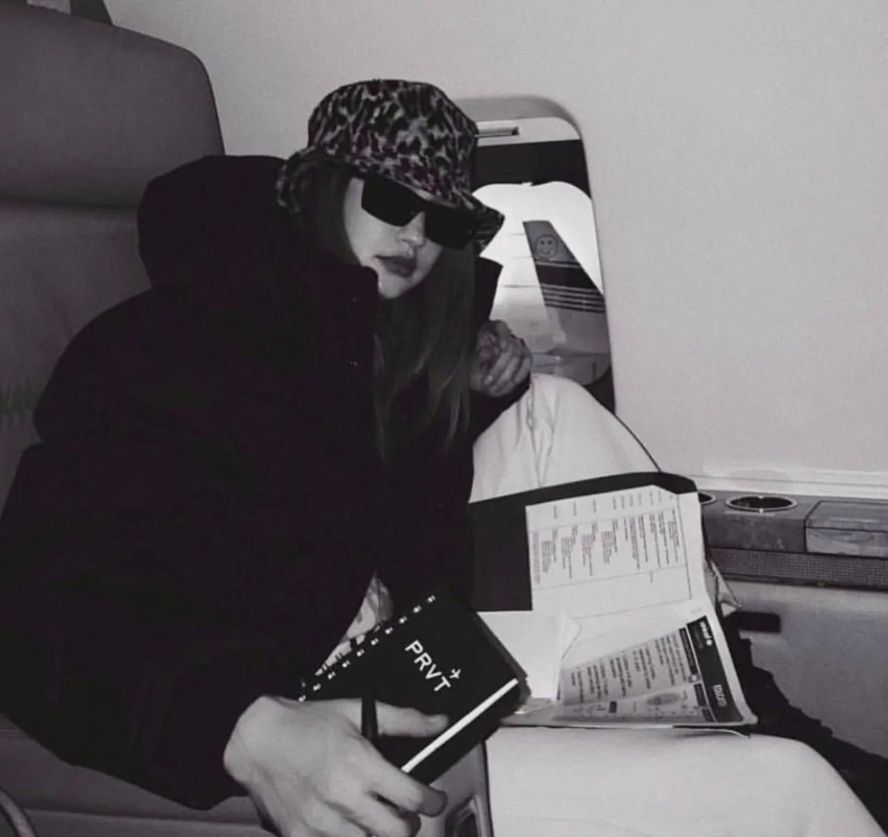 Gigi Hadid aboard a private jet holding a PRVT notebook, black-and-white brand photography for PRVT